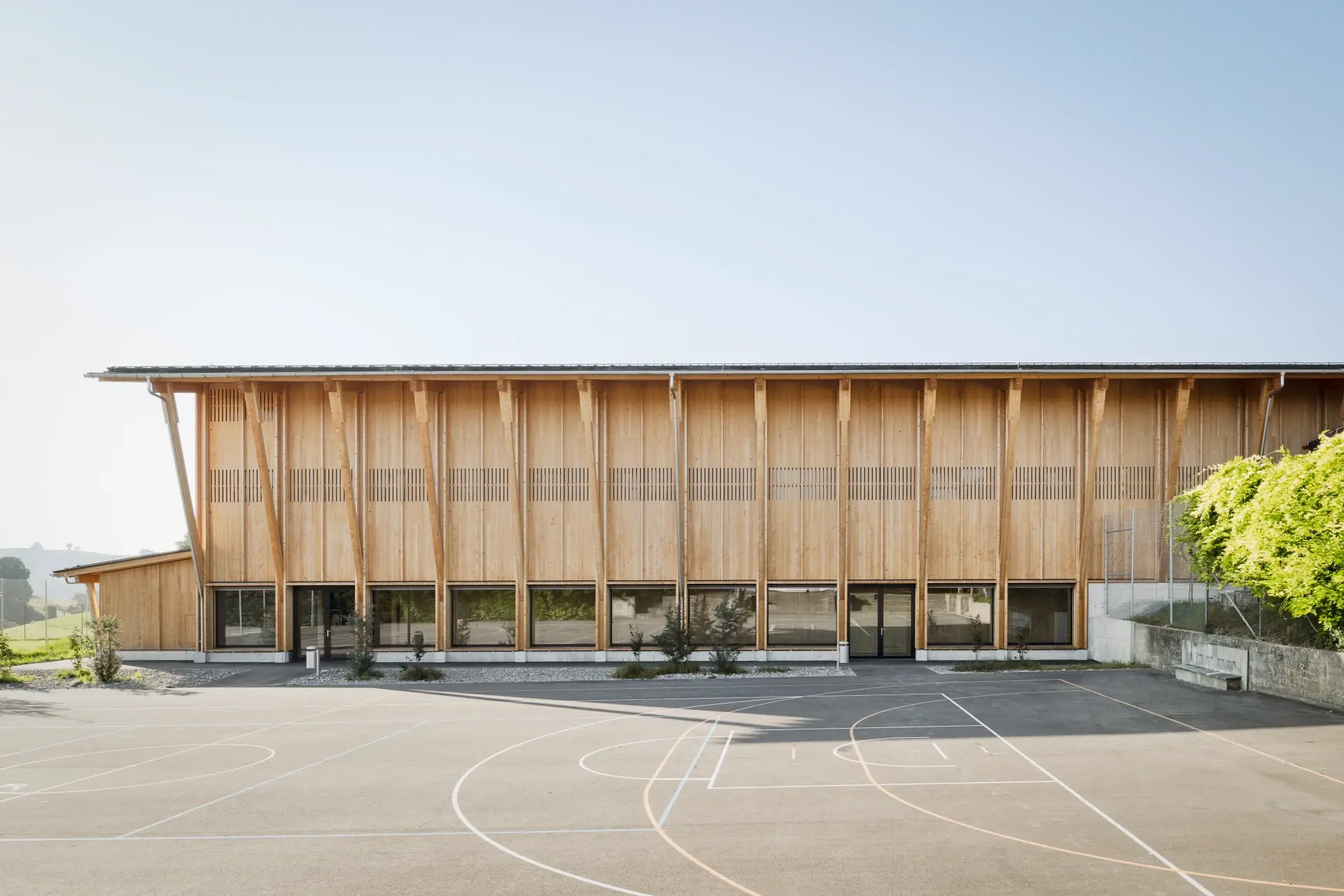 Doppelturnhalle Biglen – Aussenansicht mit Holzfassade über dem Pausenplatz
