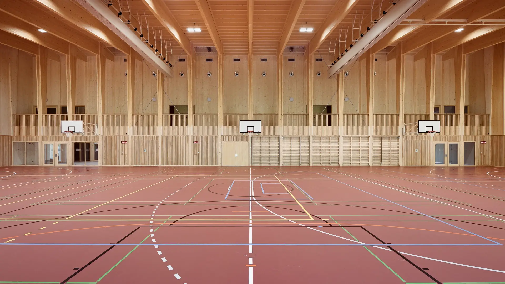 Doppelturnhalle Biglen – Innenraum mit sichtbarem Holztragwerk und Galerien
