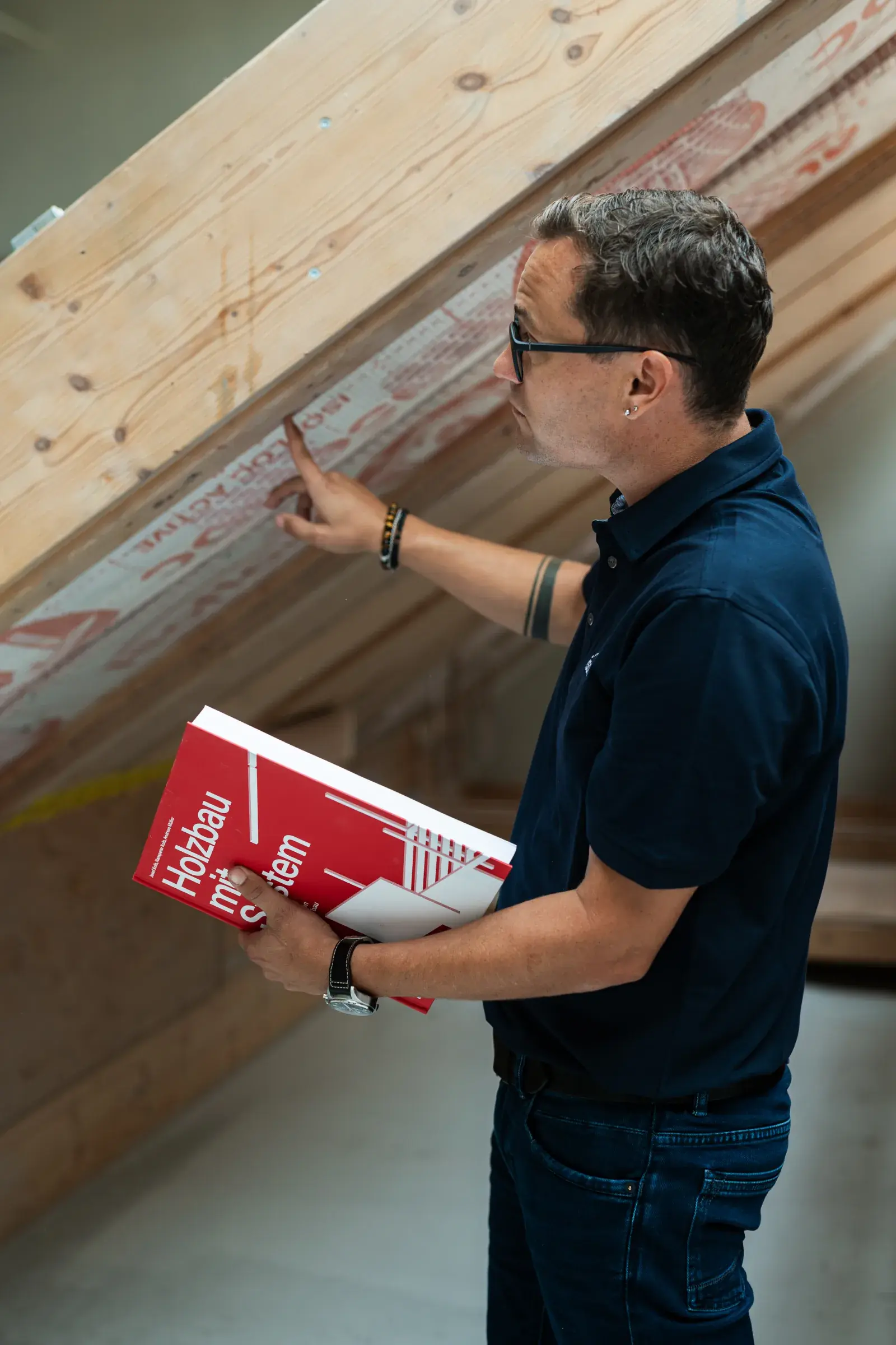 Consulente tecnico isofloc controlla una falda del tetto isolata, con in mano la brochure «Holzbau mit System»